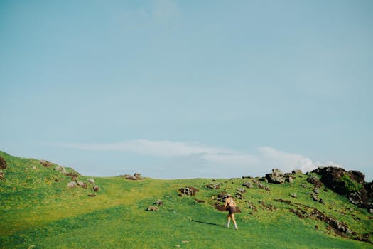 A scenic shot of a woman hiking through lush green hills on a clear day.