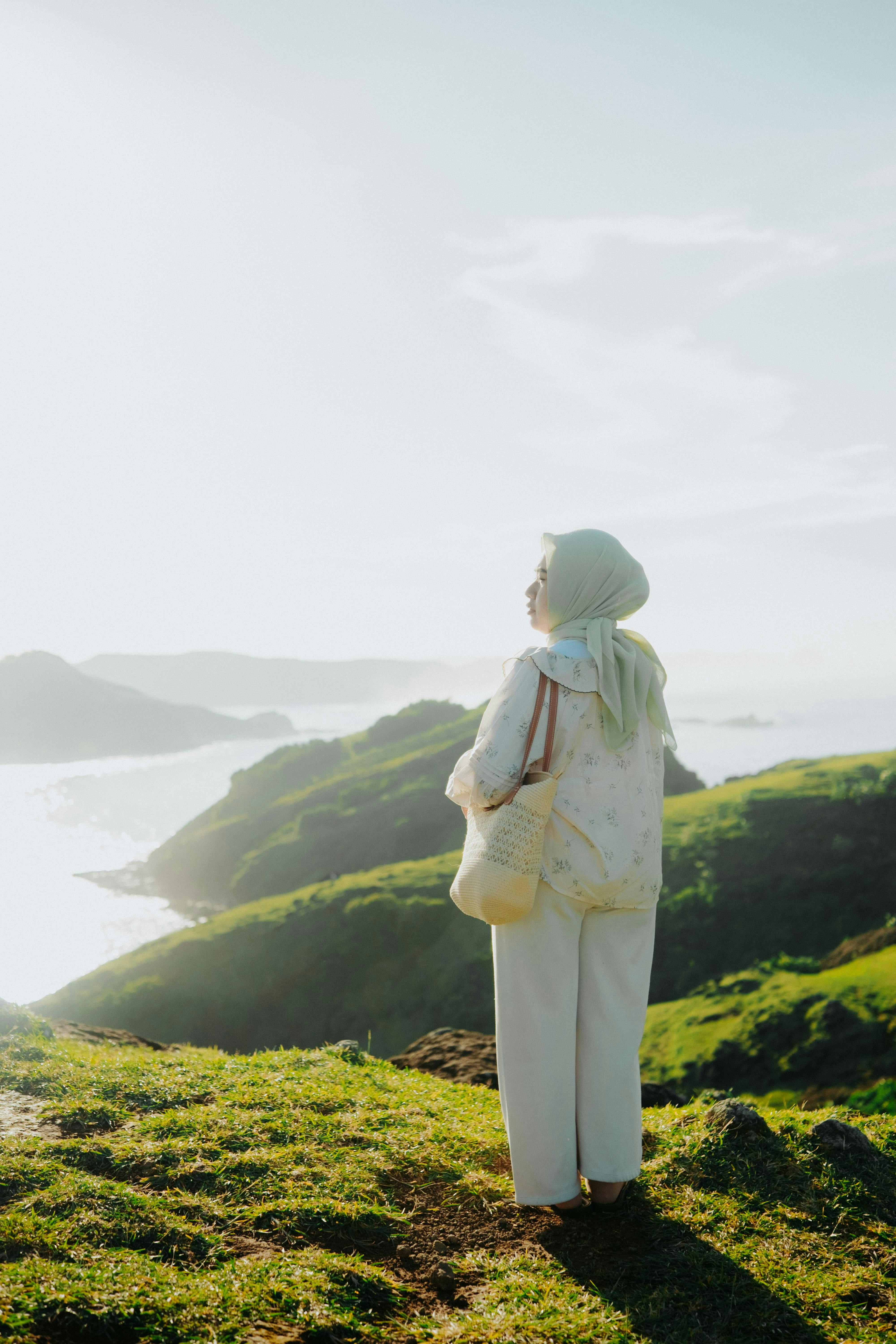 Gratis Una donna con l'hijab in piedi all'aperto, con vista sulle splendide colline verdi durante il giorno. Foto a disposizione