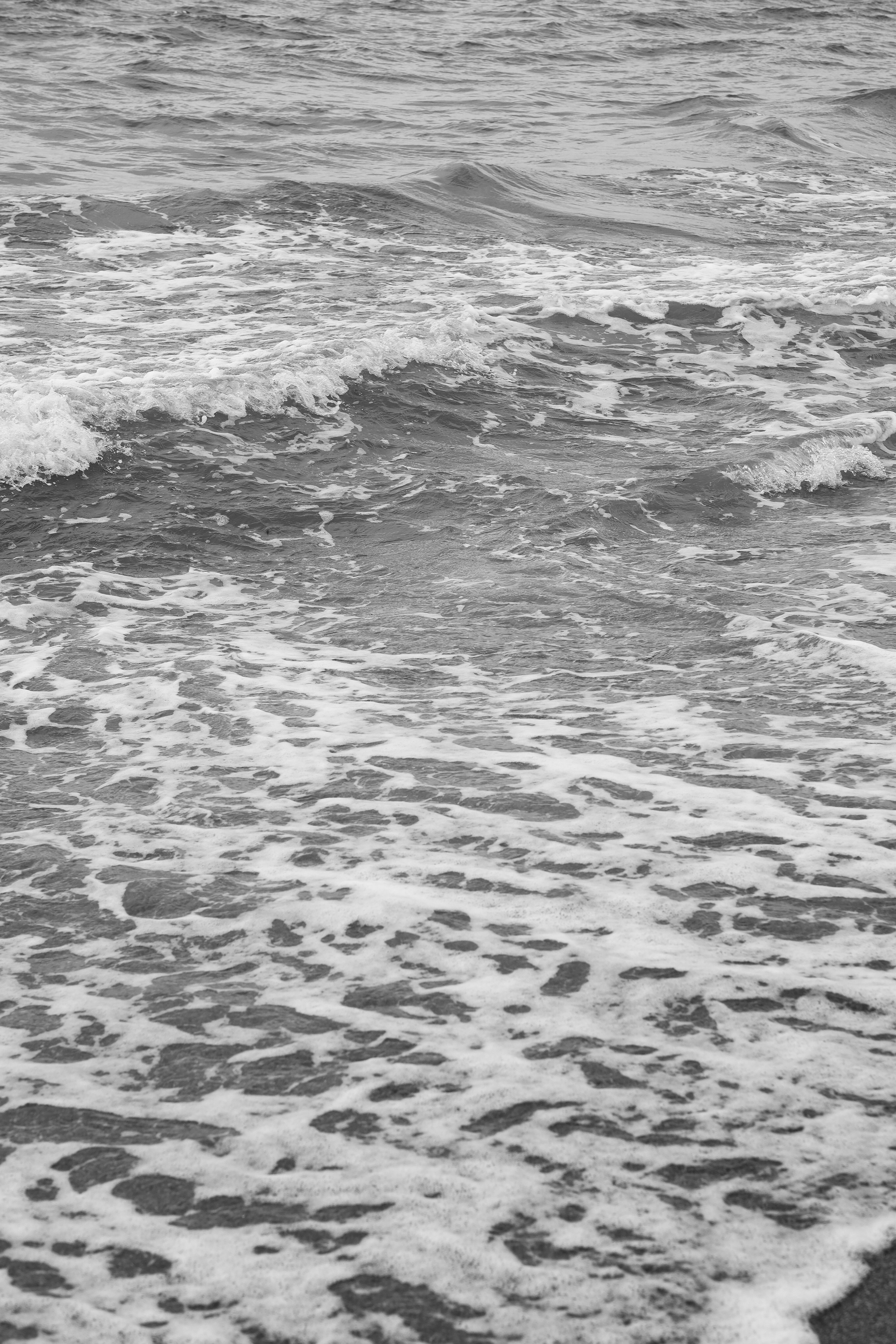 Ücretsiz Kumsalda nazikçe kıyıya vuran okyanus dalgalarının tek renkli görüntüsü, deniz suyunun dokusunu yakalıyor. Stok Fotoğraflar