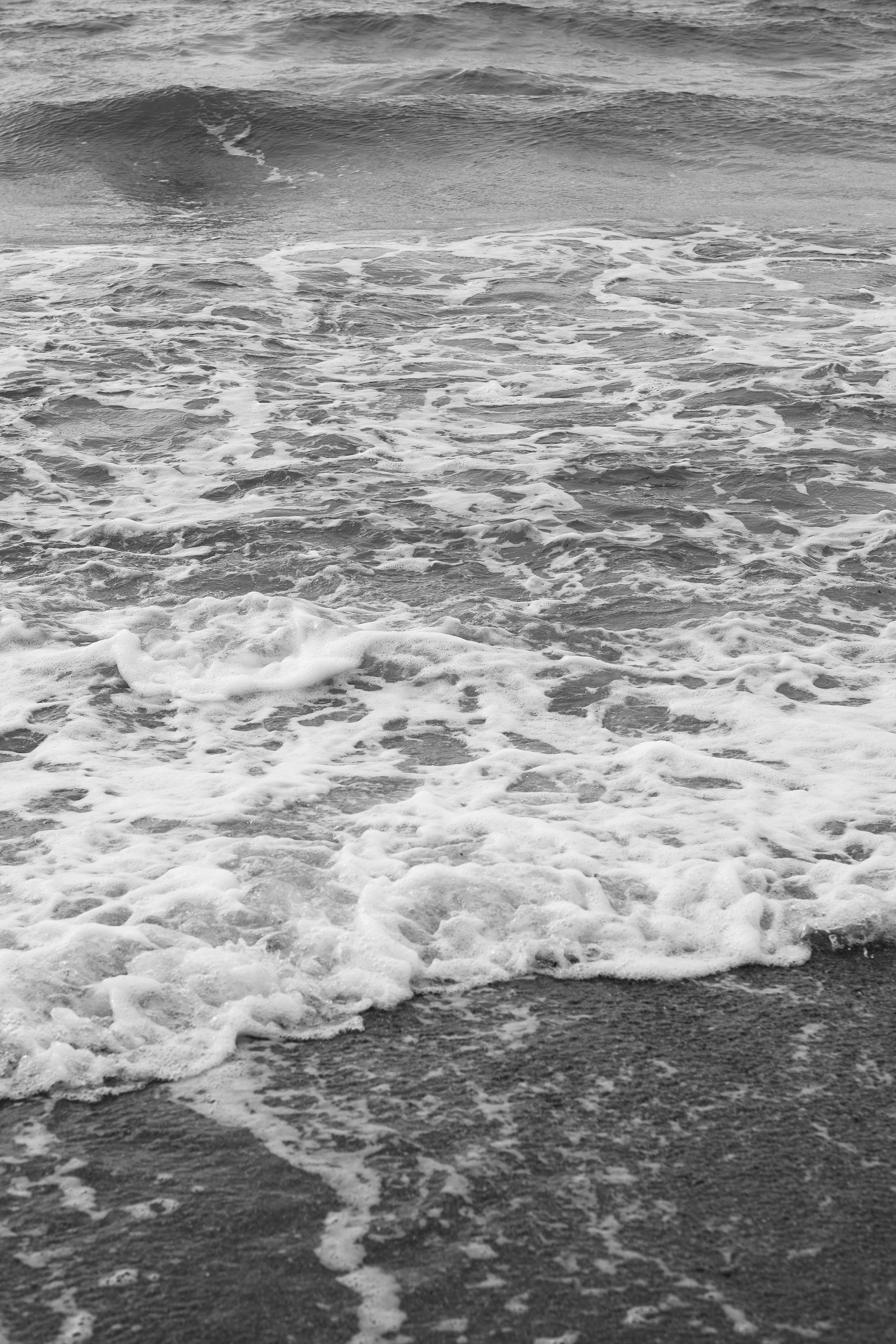 Gratuit Fotografie alb-negru a valurilor line ale oceanului care se sparg peste plaja nisipoasă într-o scenă calmă de pe litoral. Fotografie de stoc