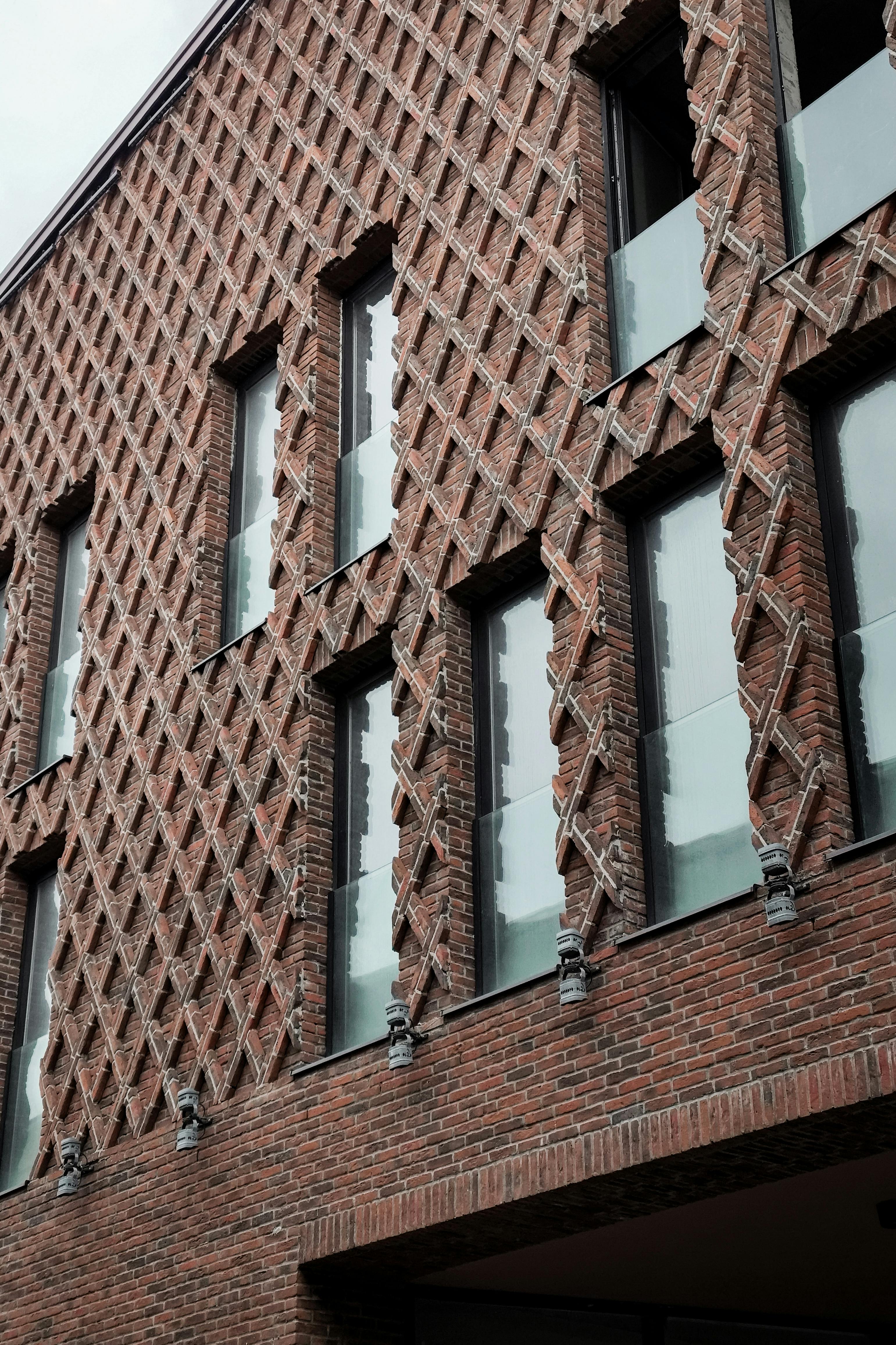 ingyenes Közeli kép egy modern téglaépületről, egyedi rácsos kialakítással és üvegerkélyekkel, amely építészeti stílust vonultat fel. Stockfotó