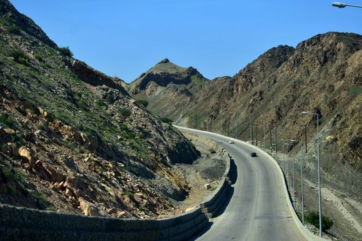 Scenic mountain road with sparse vegetation in Bandar Jissah, Oman, showcasing rugged terrain and infrastructure.