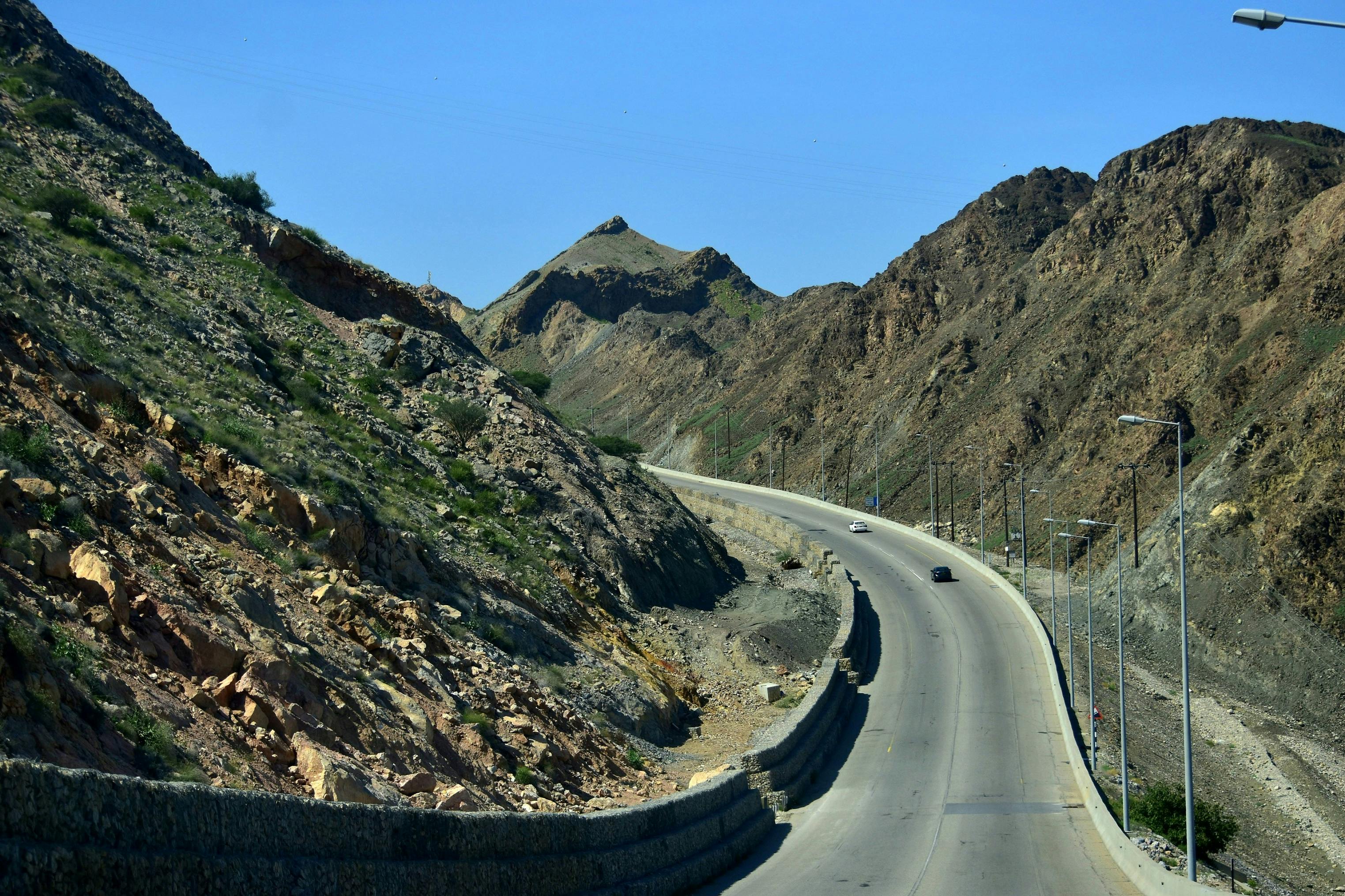 Gratis Strada panoramica di montagna con vegetazione rada a Bandar Jissah, Oman, che mette in mostra il terreno accidentato e le infrastrutture. Foto a disposizione