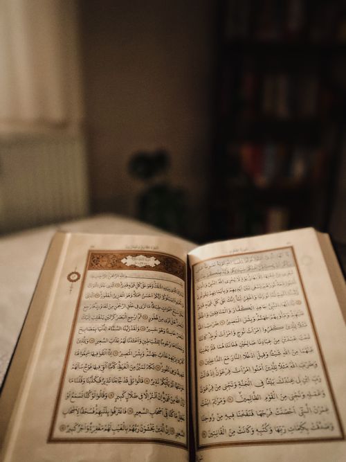 Free Close-up of an open Quran on a table, with warm lighting creating a serene atmosphere. Stock Photo