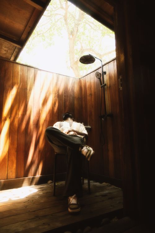 Free A person relaxing in an outdoor wooden shower with natural light filtering through the trees above. Stock Photo