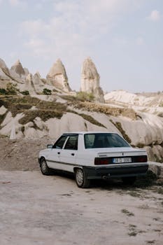 A vintage car parked amidst Cappadocia's unique rock formations in Türkiye.