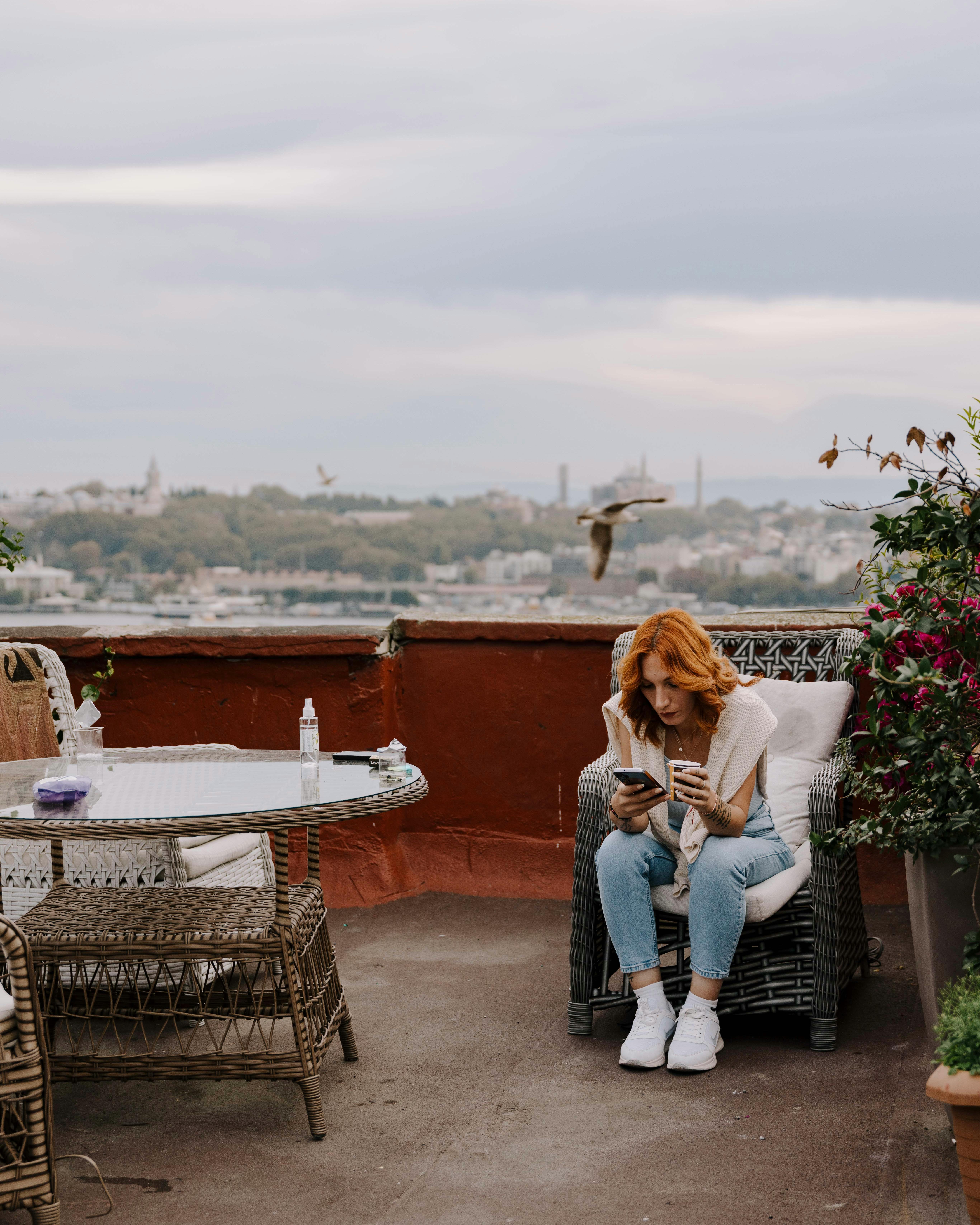 ฟรี หญิงสาวกำลังพักผ่อนบนดาดฟ้าในอิสตันบูล ประเทศตุรกี พร้อมชมวิวเมืองและต้นไม้ บันทึกช่วงเวลาอันสงบสุขกลางแจ้ง คลังภาพถ่าย