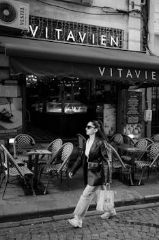 Black and white photo of a woman walking past a cafe in Türkiye, exuding urban elegance.