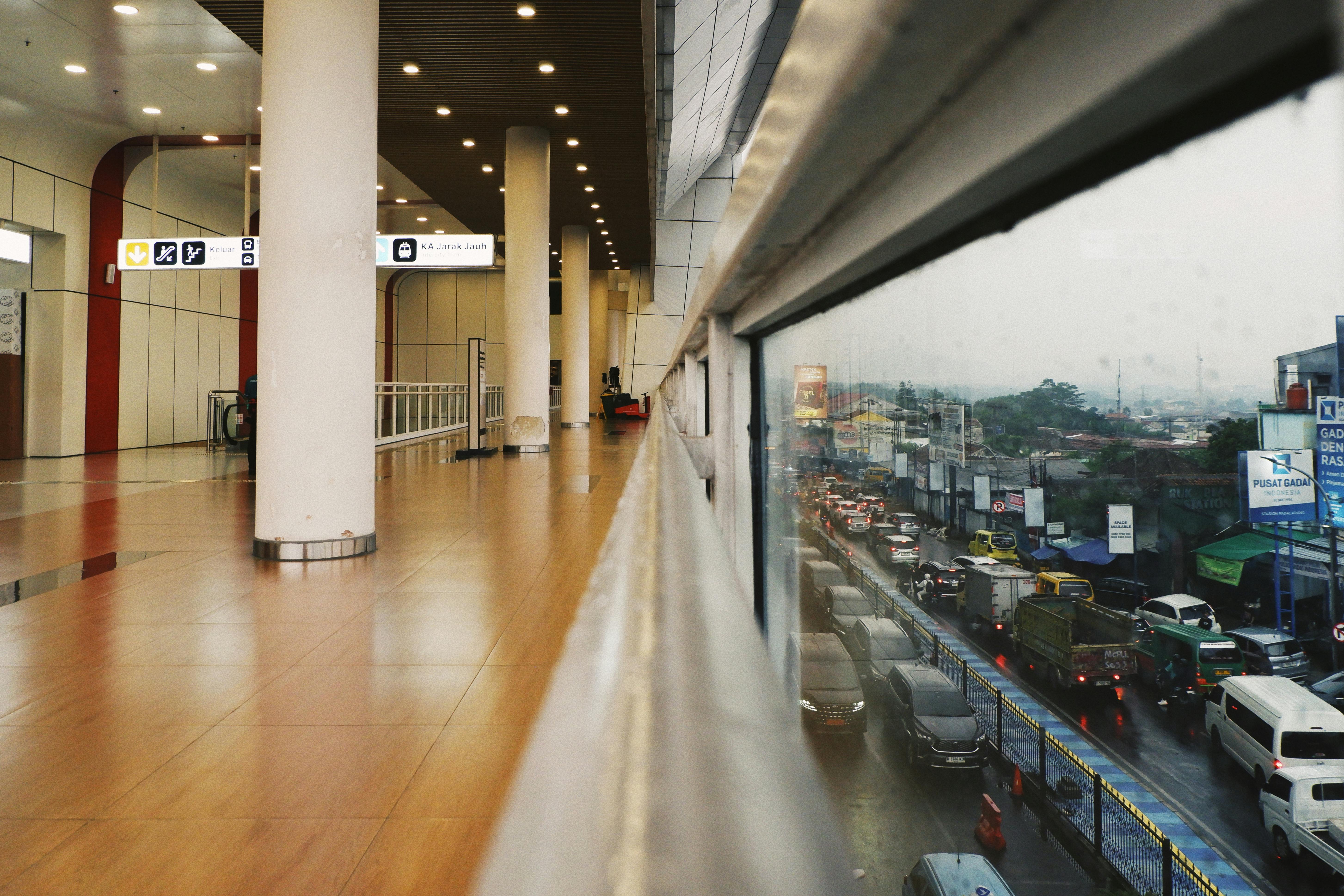 Gratis Lorong dalam ruangan modern dengan pemandangan lalu lintas jalanan yang ramai melalui jendela besar, menangkap kontras kehidupan perkotaan. Foto Stok