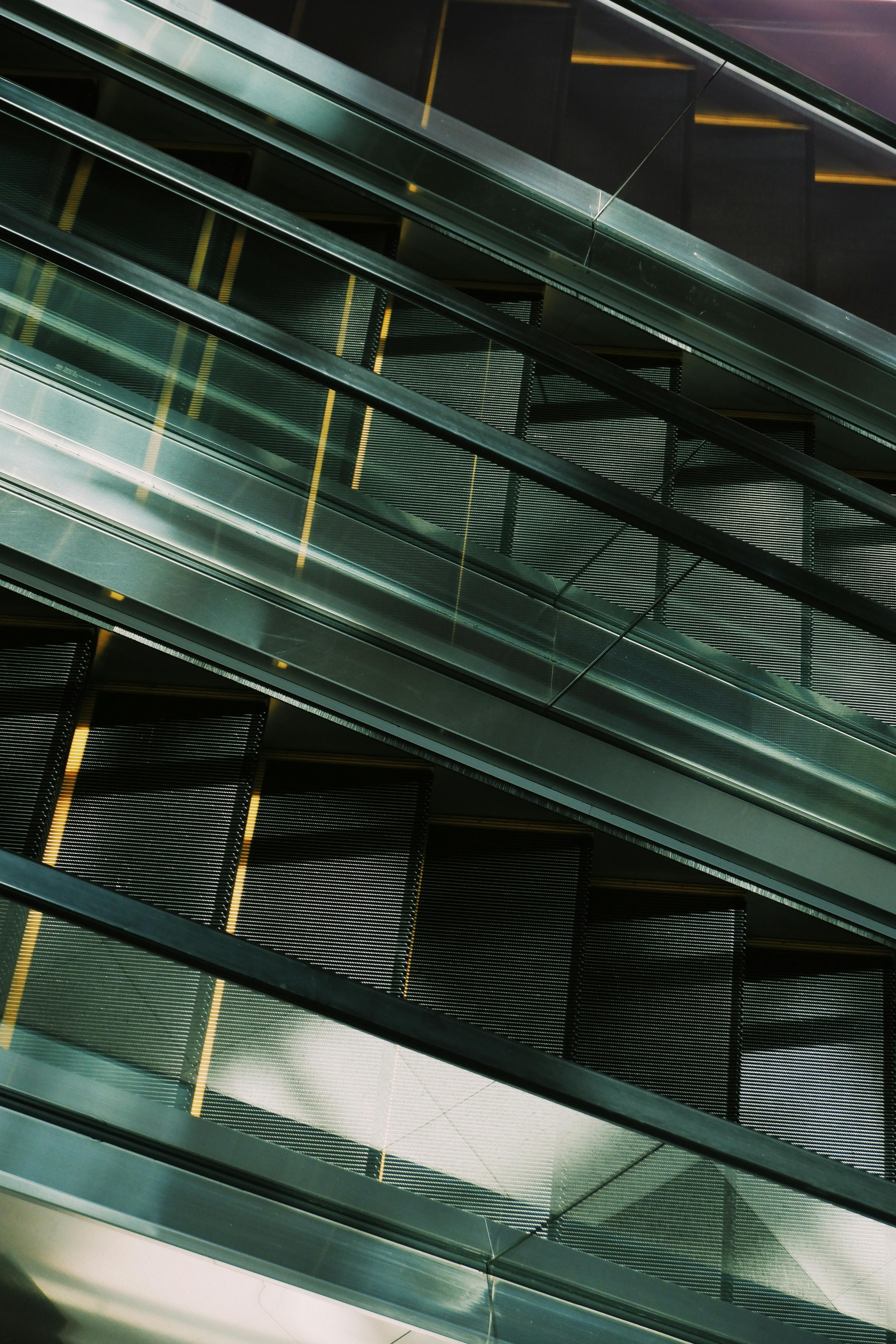 Free A modern escalator system inside a shopping mall with geometric patterns and glass reflections. Stock Photo