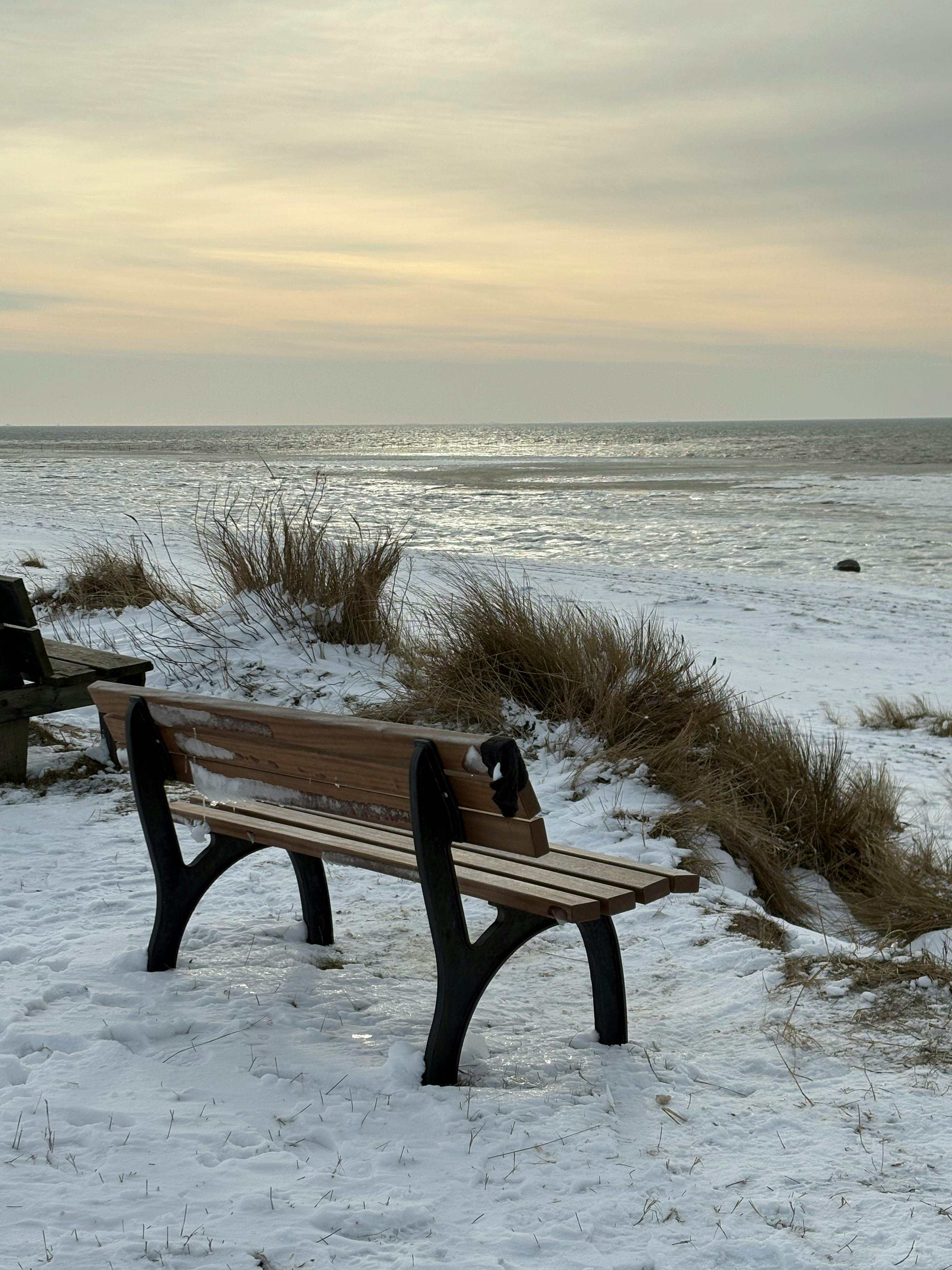 Gratis Tranquilla spiaggia innevata nello Schleswig-Holstein, in Germania, con panchine sotto un sereno tramonto. Foto a disposizione