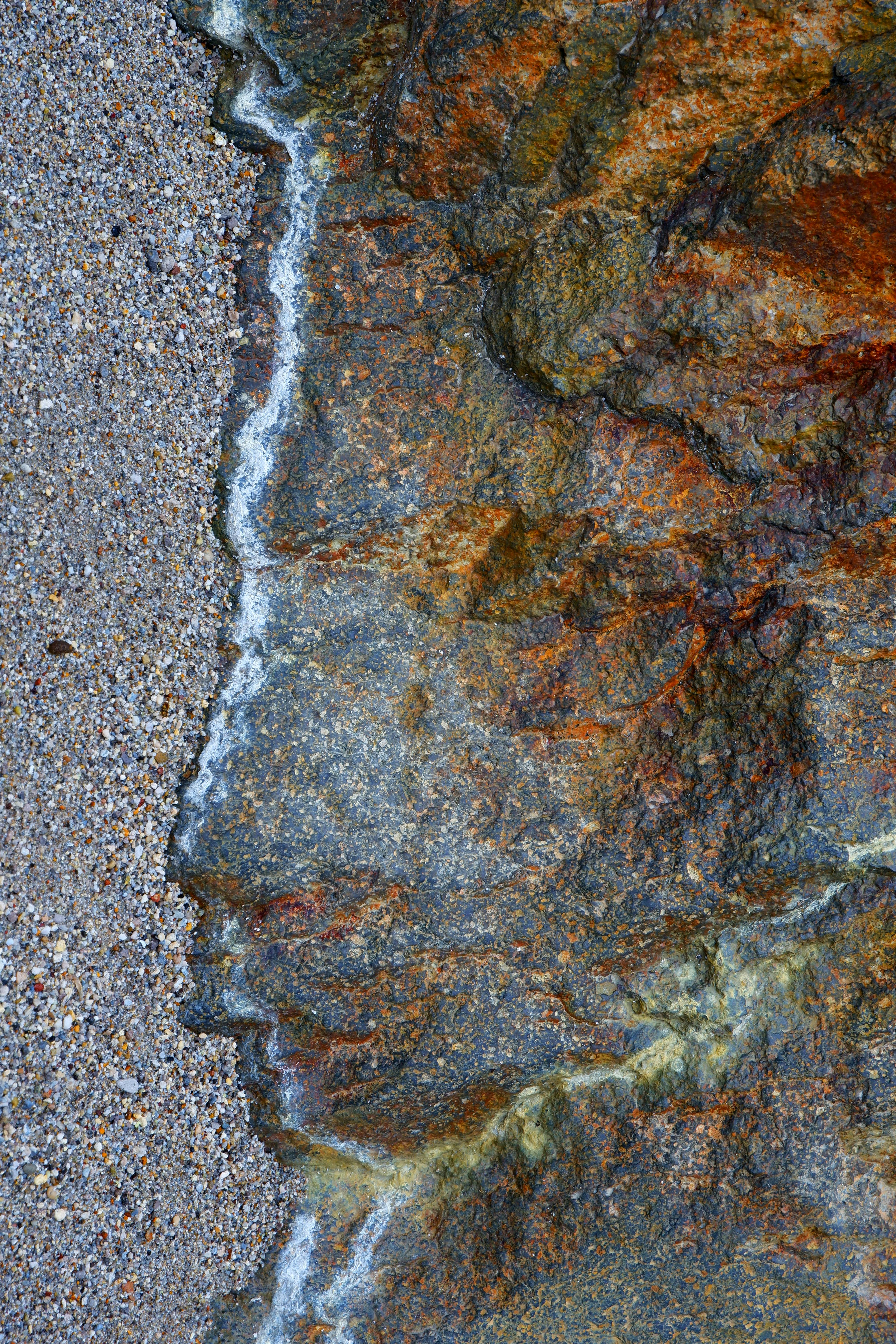 gratis Close-up van een rotsachtige kustlijn met schuimende zee en een zandstrand, waarop de natuurlijke texturen en kleuren te zien zijn. Stockfoto