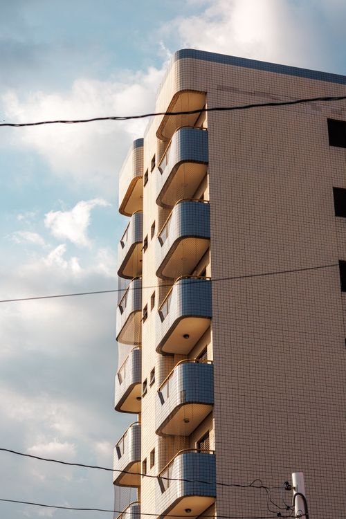 Free Sunlit modern residential building with balconies against a cloudy sky, showcasing urban architecture. Stock Photo