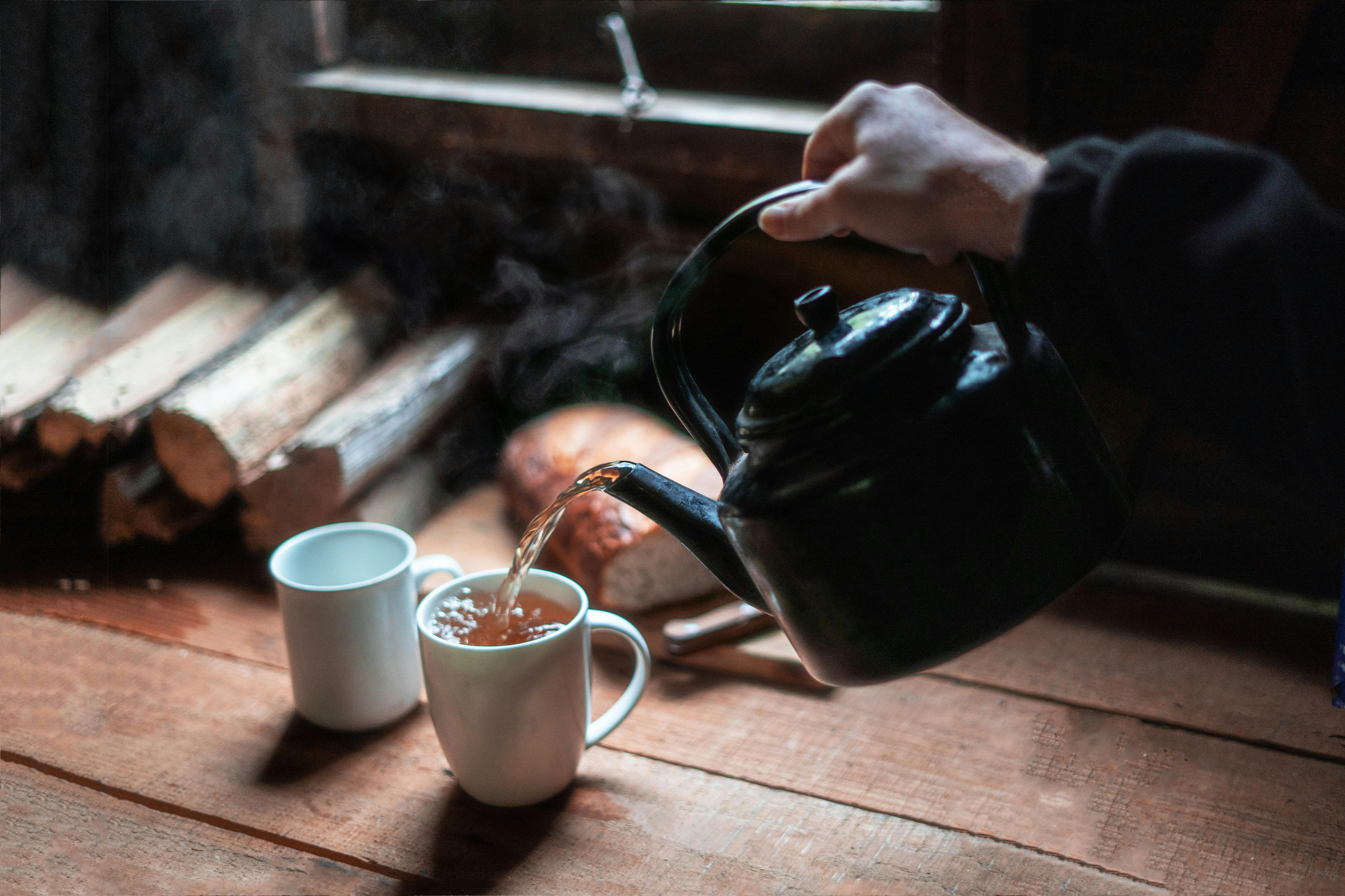 person pouring tea in white ceramic mug