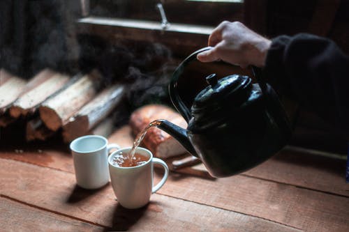 白いセラミックマグカップにお茶を注ぐ人