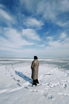 A lone person stands on a vast, snowy landscape under a clear blue sky in Konaev, Kazakhstan.
