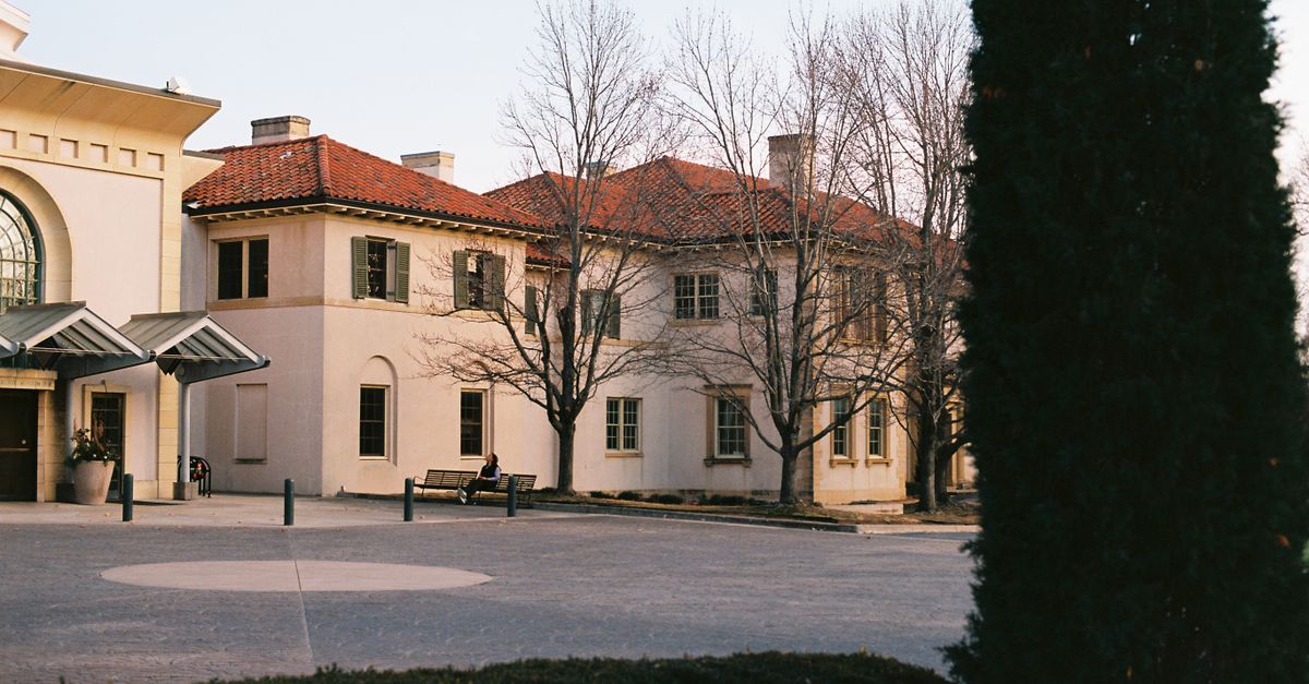An elegant historic building with a red tiled roof and bare winter trees in front.