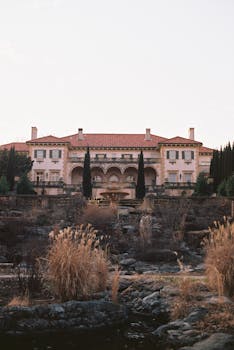 A grand Mediterranean-style villa surrounded by a formal garden and cypress trees.