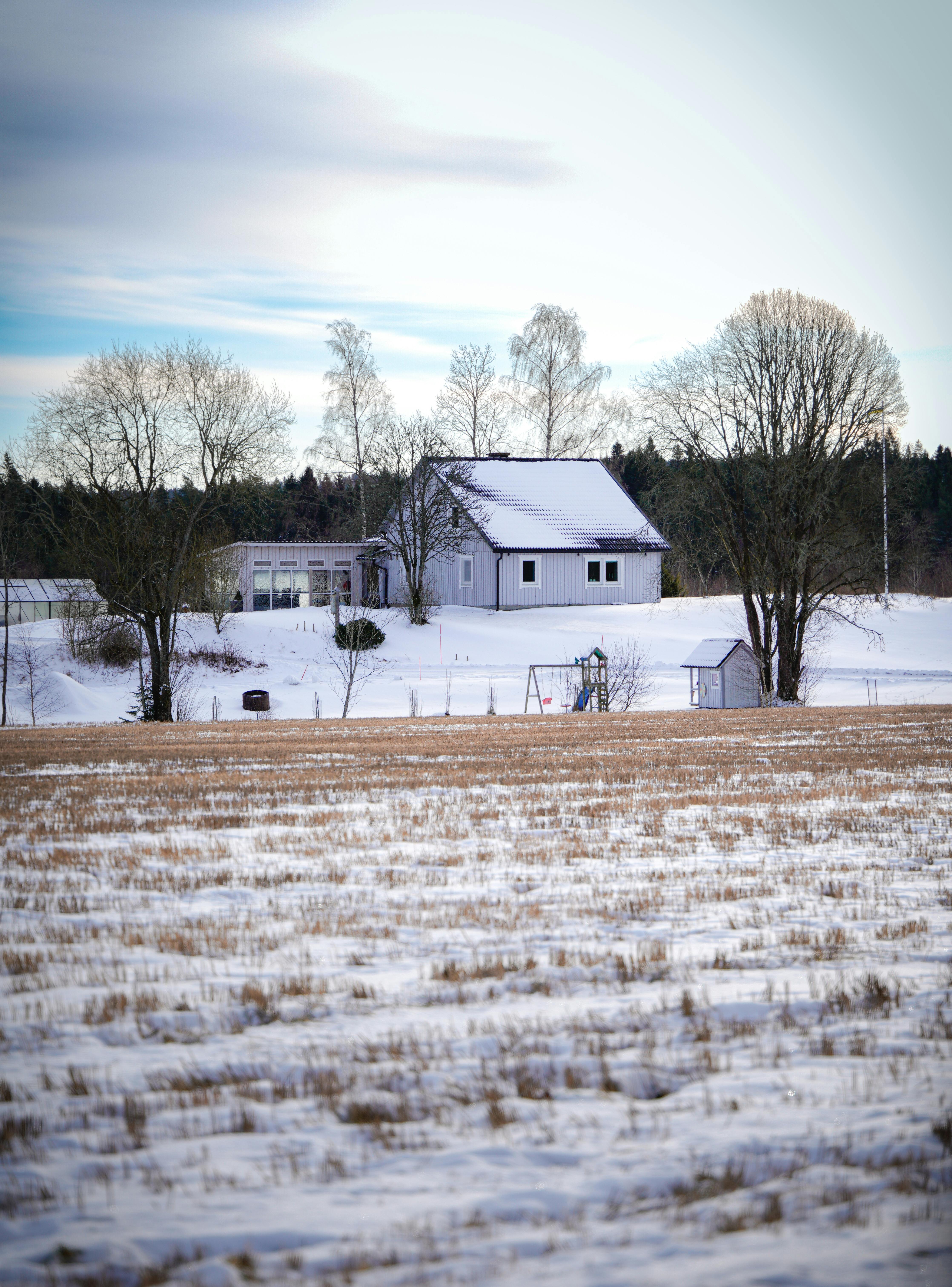 ฟรี ภาพทิวทัศน์ชนบทอันเงียบสงบปกคลุมด้วยหิมะ มีบ้านและต้นไม้ตั้งอยู่ คลังภาพถ่าย