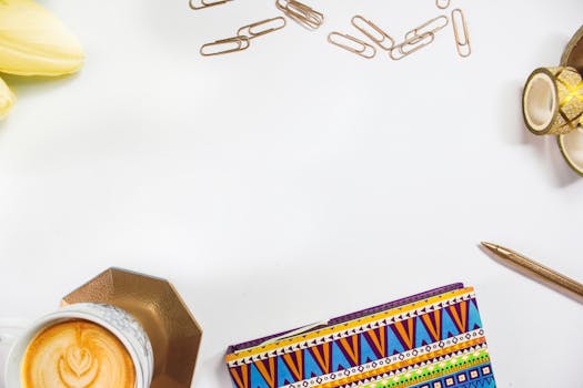 A vibrant workspace with a colorful notebook, coffee, and stationery on a white background, perfect for inspiration.