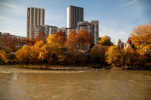 View of high-rise buildings and colorful autumn foliage along a river in Tbilisi, Georgia.