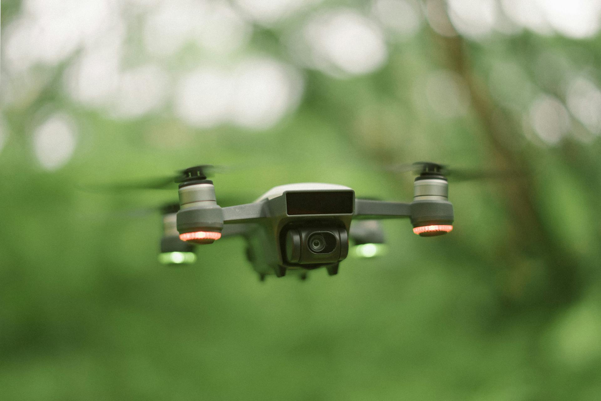 A drone with red and green lights hovers in a lush green environment.