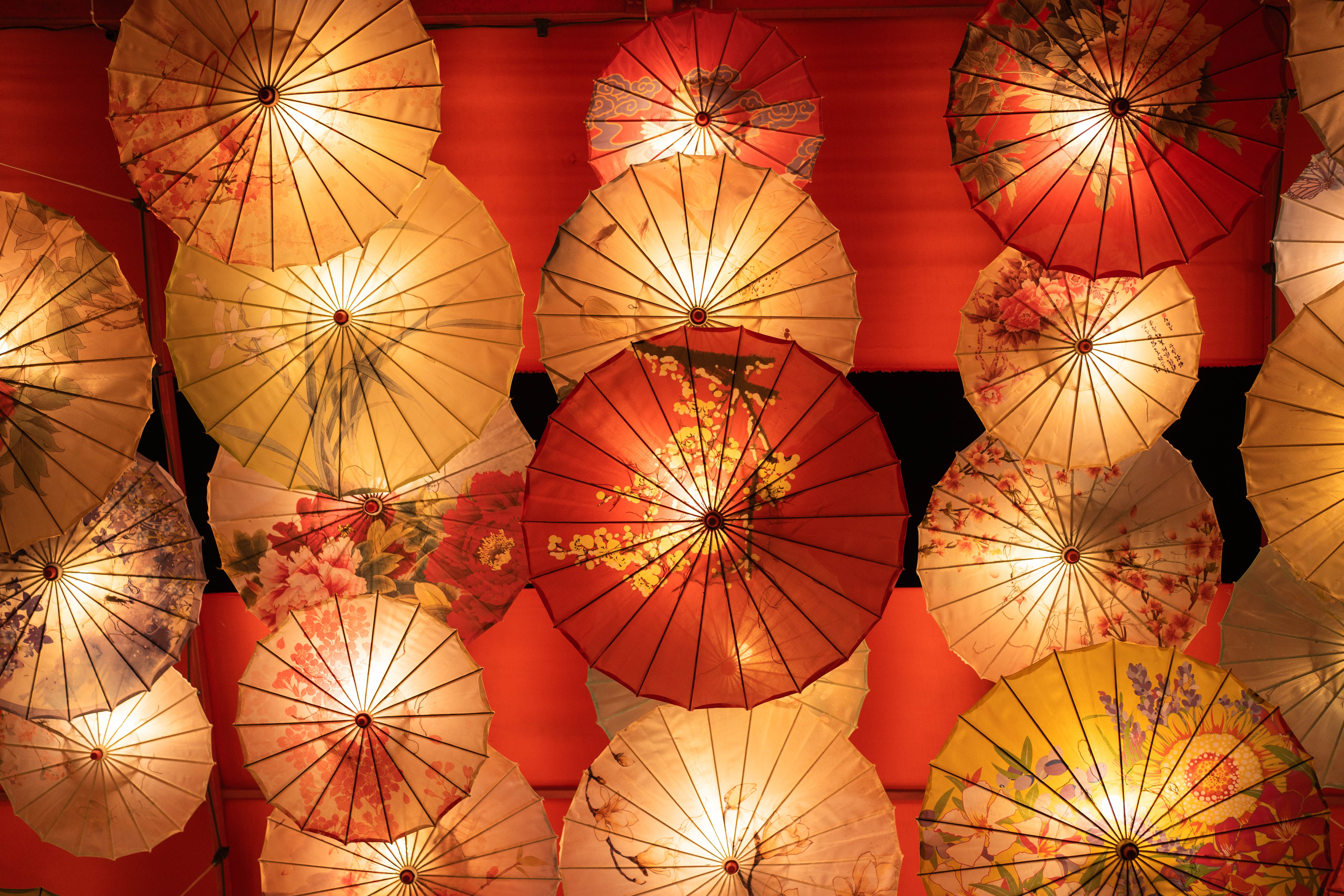 Vibrant assortment of illuminated Asian-style umbrellas with intricate floral patterns, creating a stunning decorative display.
