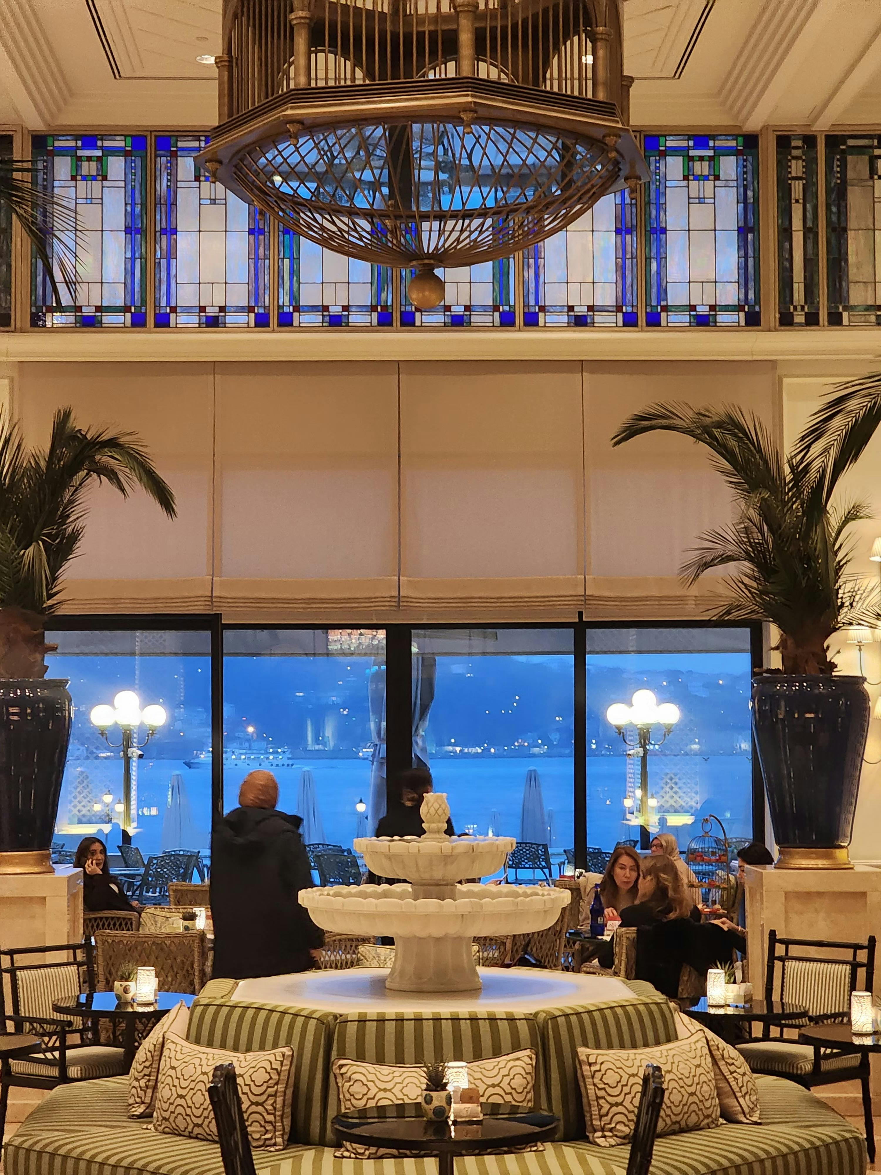 Gratis Lussuosa lounge dell'hotel con un'elegante fontana, vetrate colorate e splendide finestre con vista sulla città. Foto a disposizione