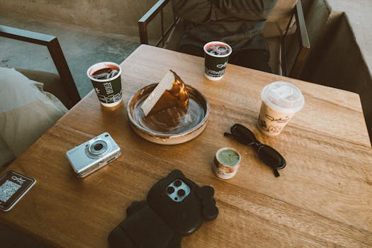 A relaxing scene with coffee, cake, and a camera on a wooden table at an Oman cafe.