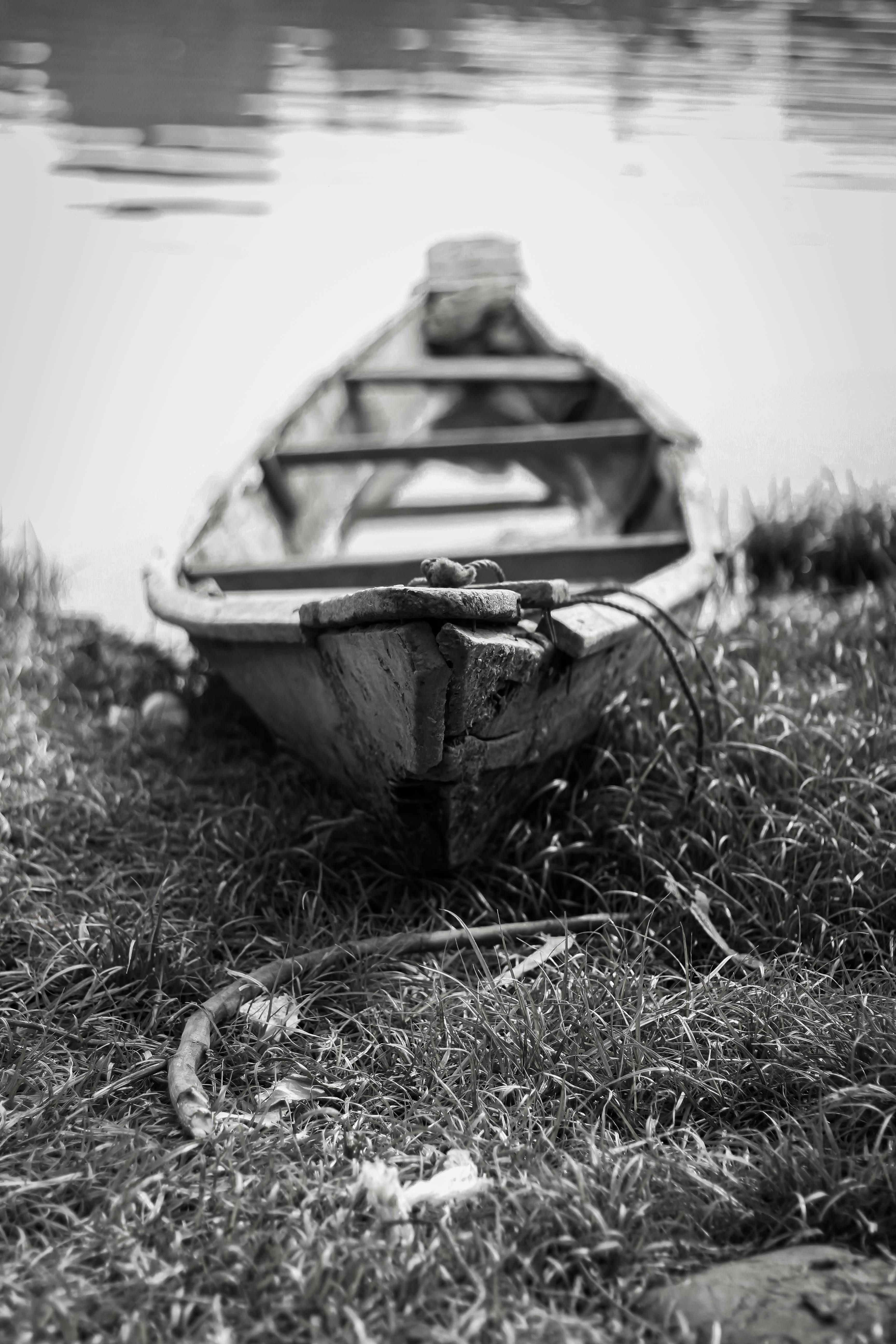 Gratis Un bote de remos antiguo y desgastado descansa en la orilla cubierta de hierba del río, capturado en blanco y negro. Foto de stock