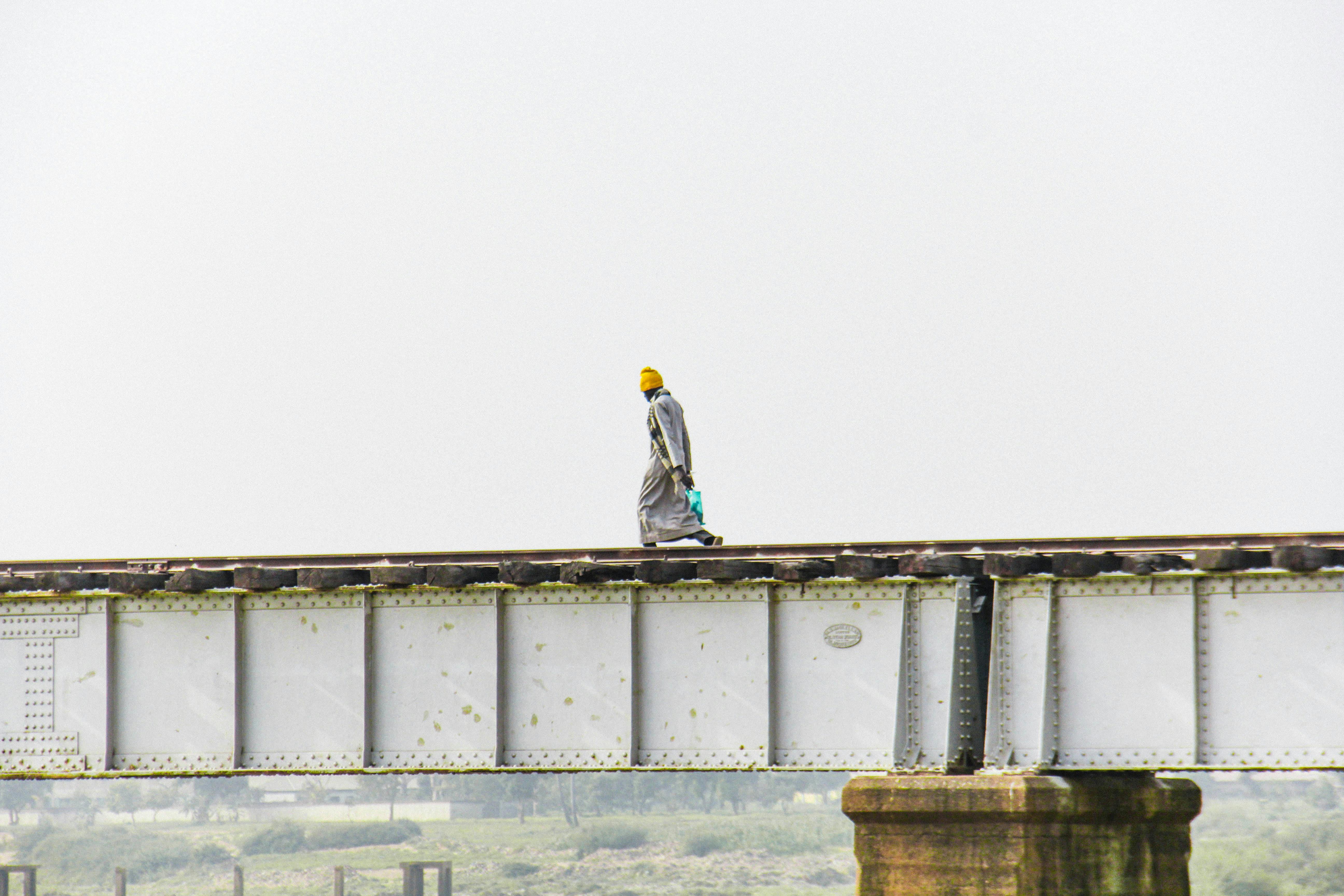 Gratis Una figura solitaria cammina su un ponte ferroviario contro un cielo limpido. Concetto di solitudine e viaggio. Foto a disposizione