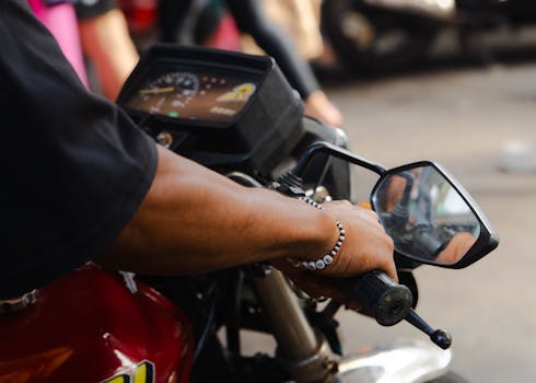 Close-up of a person's hand on a motorcycle handlebar outdoors, showcasing control and style.