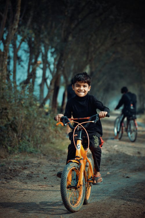 Gratis Anak Laki Laki Berkemeja Hitam Lengan Panjang Mengendarai Sepeda Oranye Foto Stok