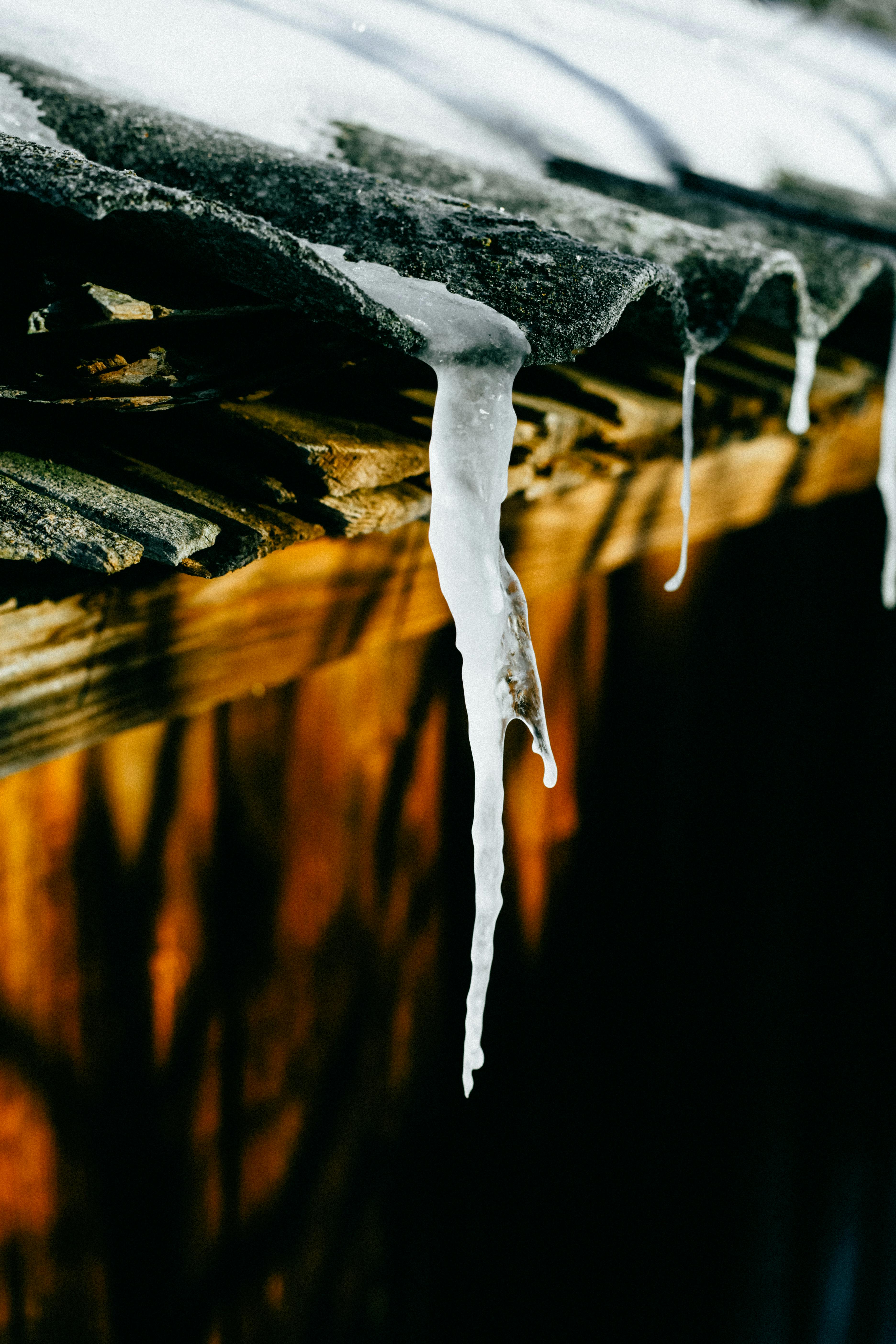 Gratis Primo piano di ghiaccioli su un tetto di legno, che riflettono la luce del sole in una scena invernale. Foto a disposizione