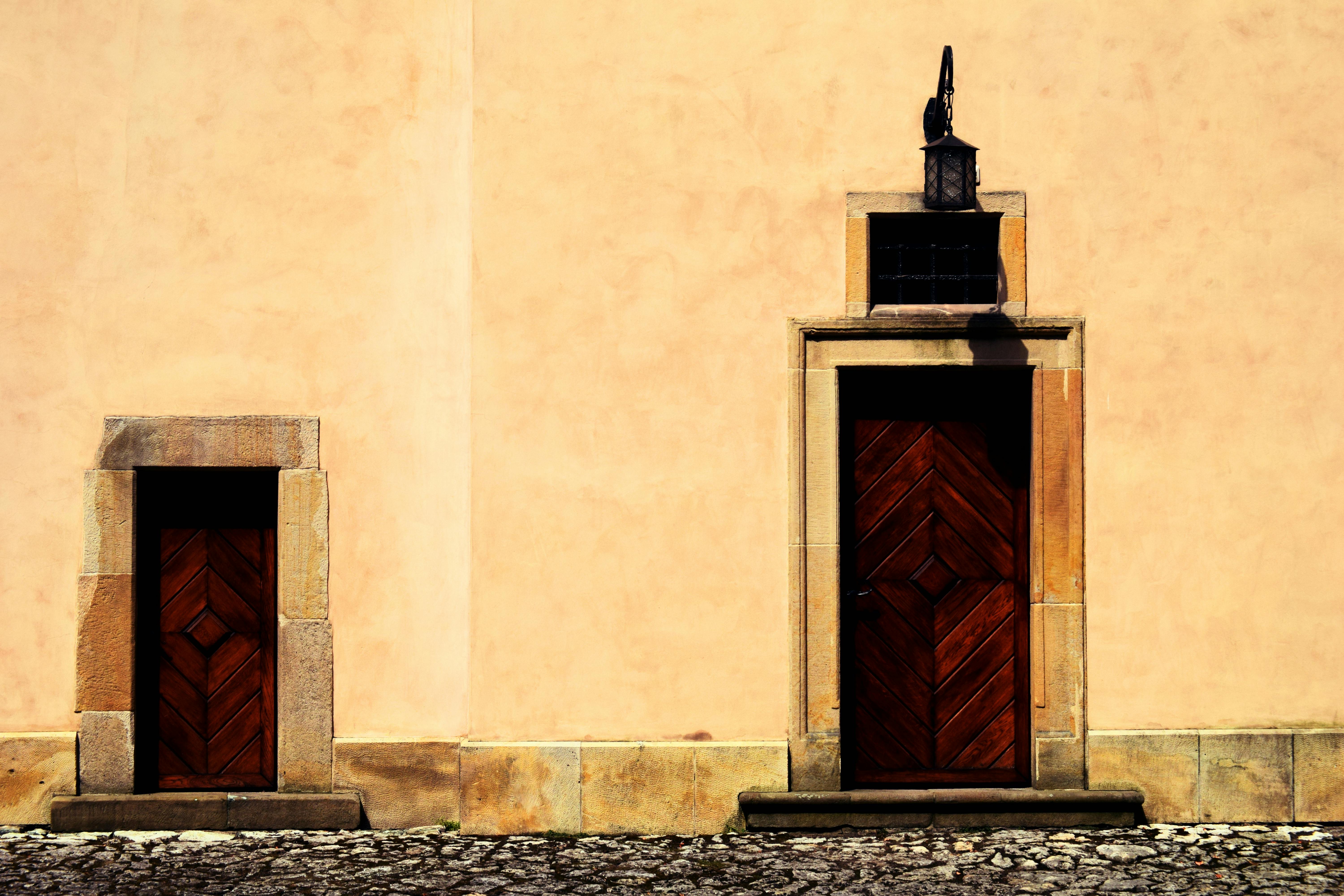 Gratis Due porte rustiche in legno su una parete beige testurizzata con una lanterna d'epoca. Foto a disposizione