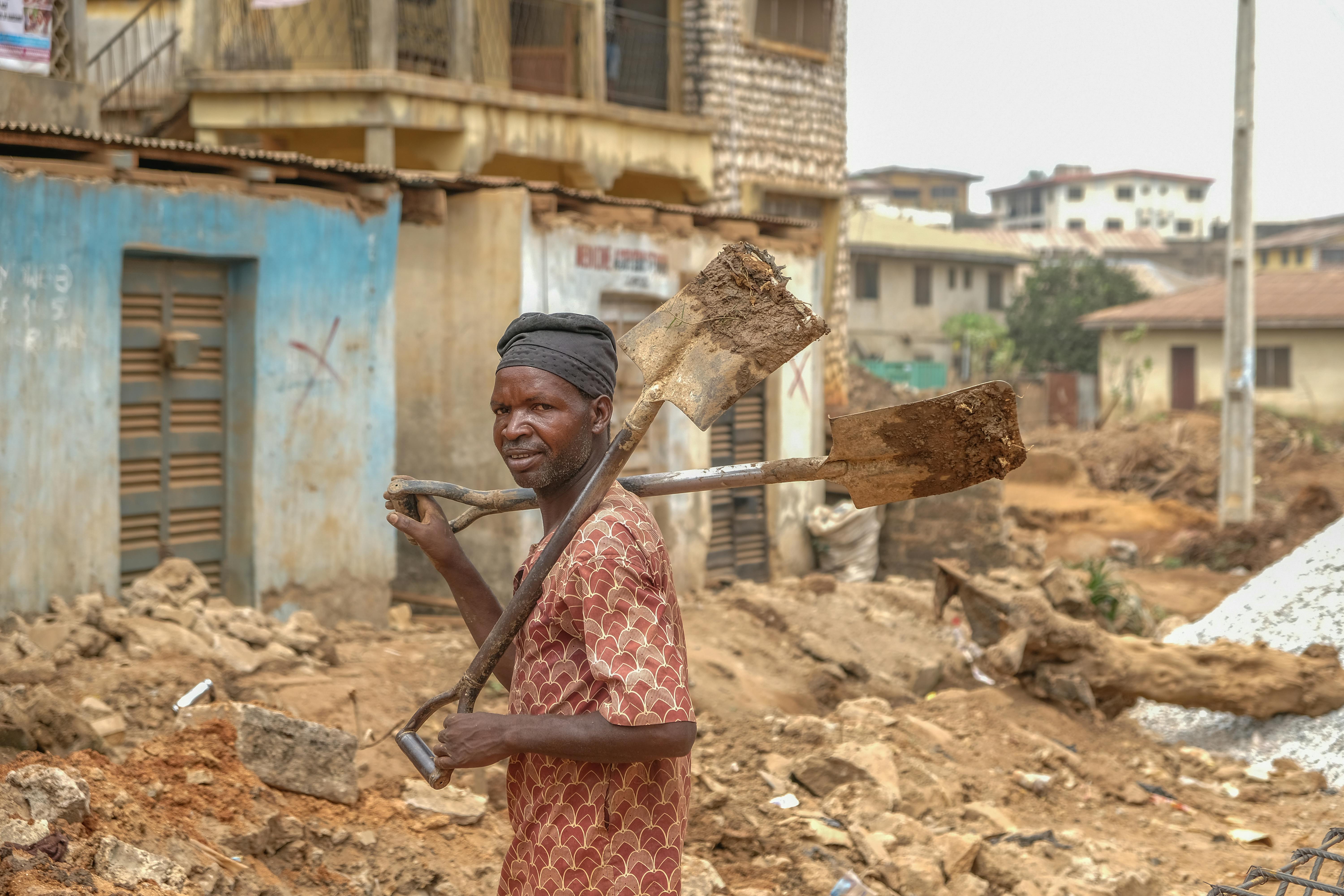 Gratis Un operaio edile che trasporta delle pale in una strada di Ife, in Nigeria, mostra lo sviluppo urbano locale. Foto a disposizione