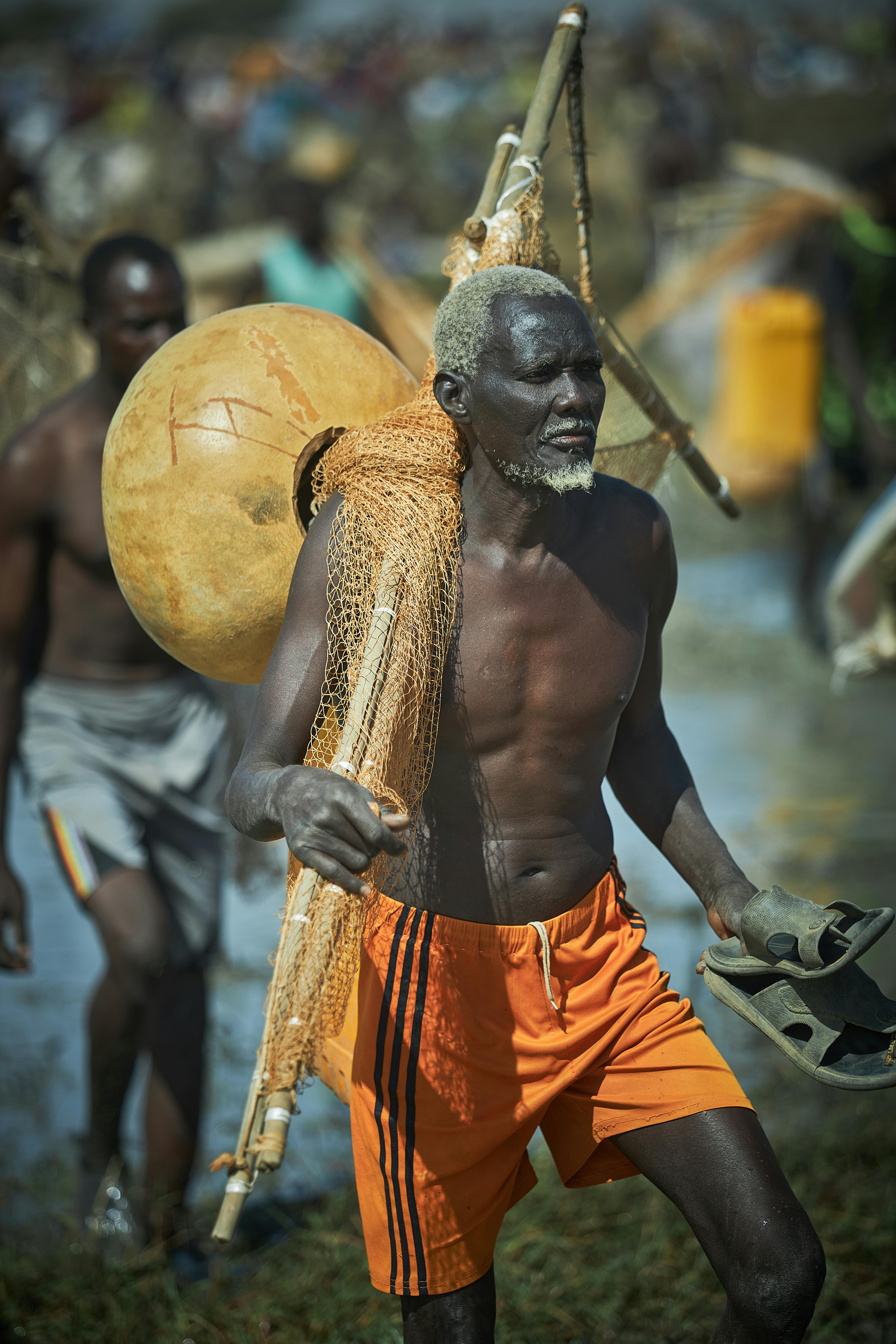 ฟรี ภาพถ่ายของชาวประมงสูงอายุคนหนึ่งกำลังแบกแหและอุปกรณ์จับปลาแบบดั้งเดิมออกไปริมน้ำ คลังภาพถ่าย