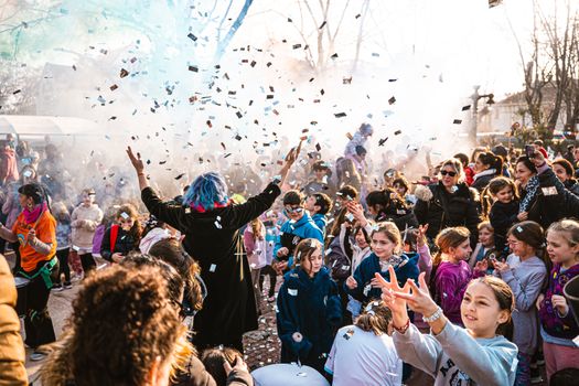 A vibrant outdoor celebration with kids enjoying confetti and performers.