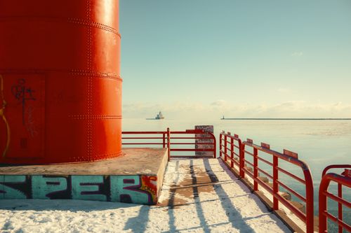 Free Vibrant red lighthouse on a snowy pier with a serene winter seascape background. Stock Photo