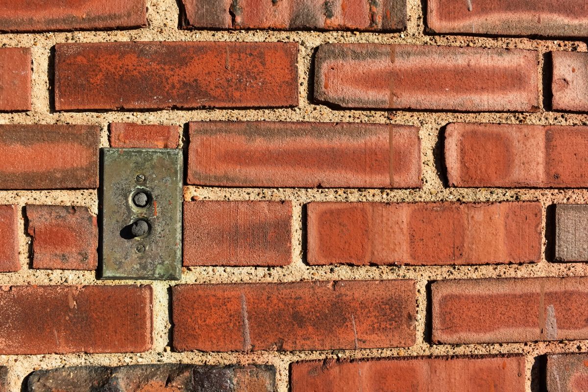 An antique push-button light switch plate set into red Chicago-style brick