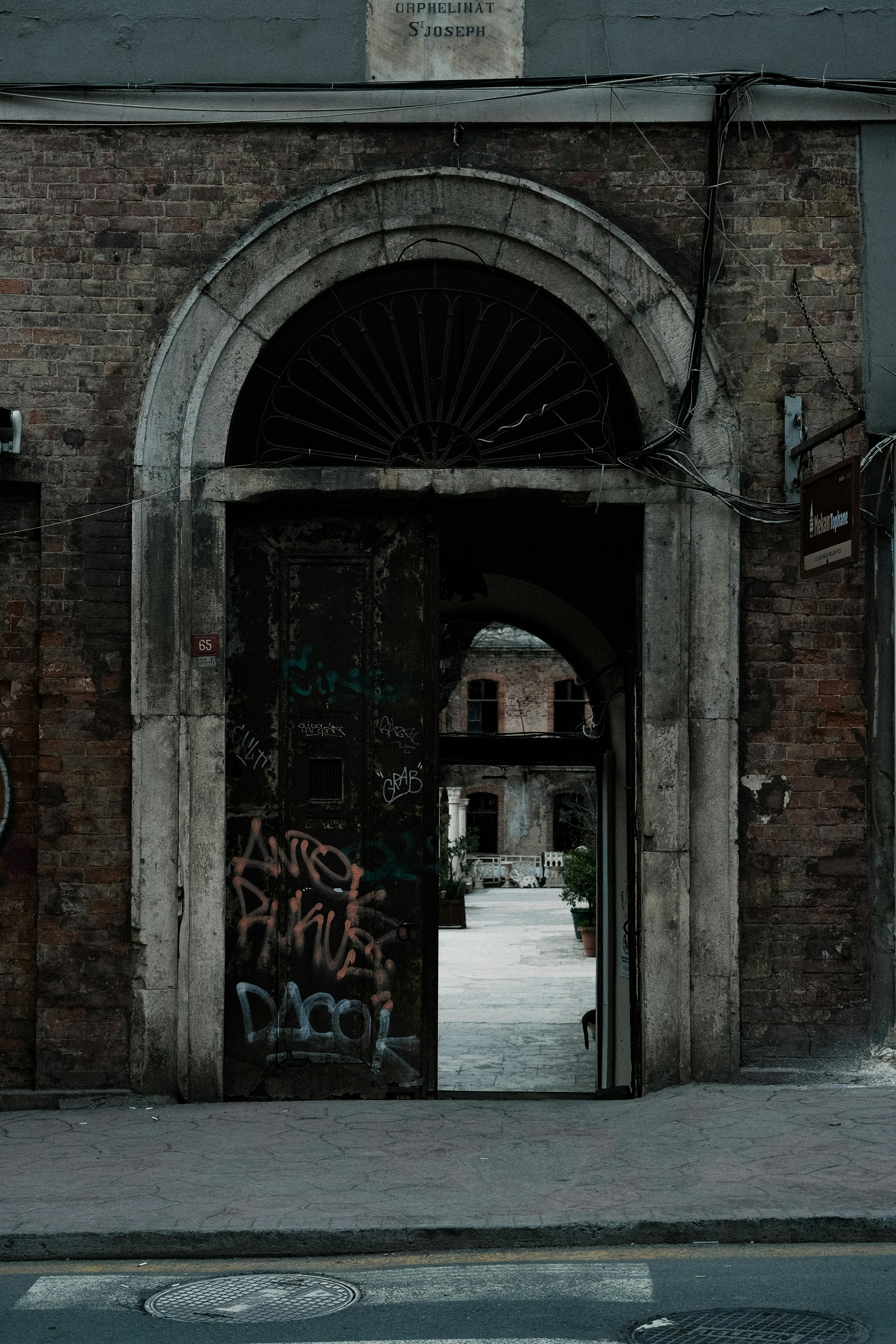 Gratuit Arcă veche din piatră cu graffiti duce spre o curte pietruită cu vedere Fotografie de stoc