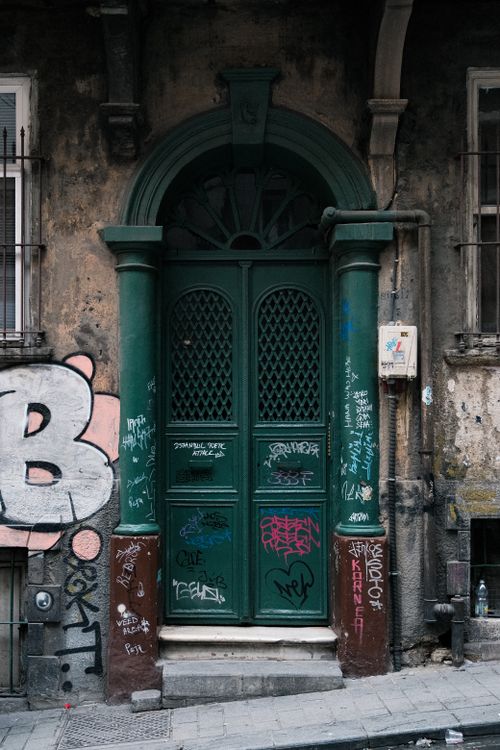 Free A rustic green door with detailed urban graffiti in a vintage European street setting. Stock Photo