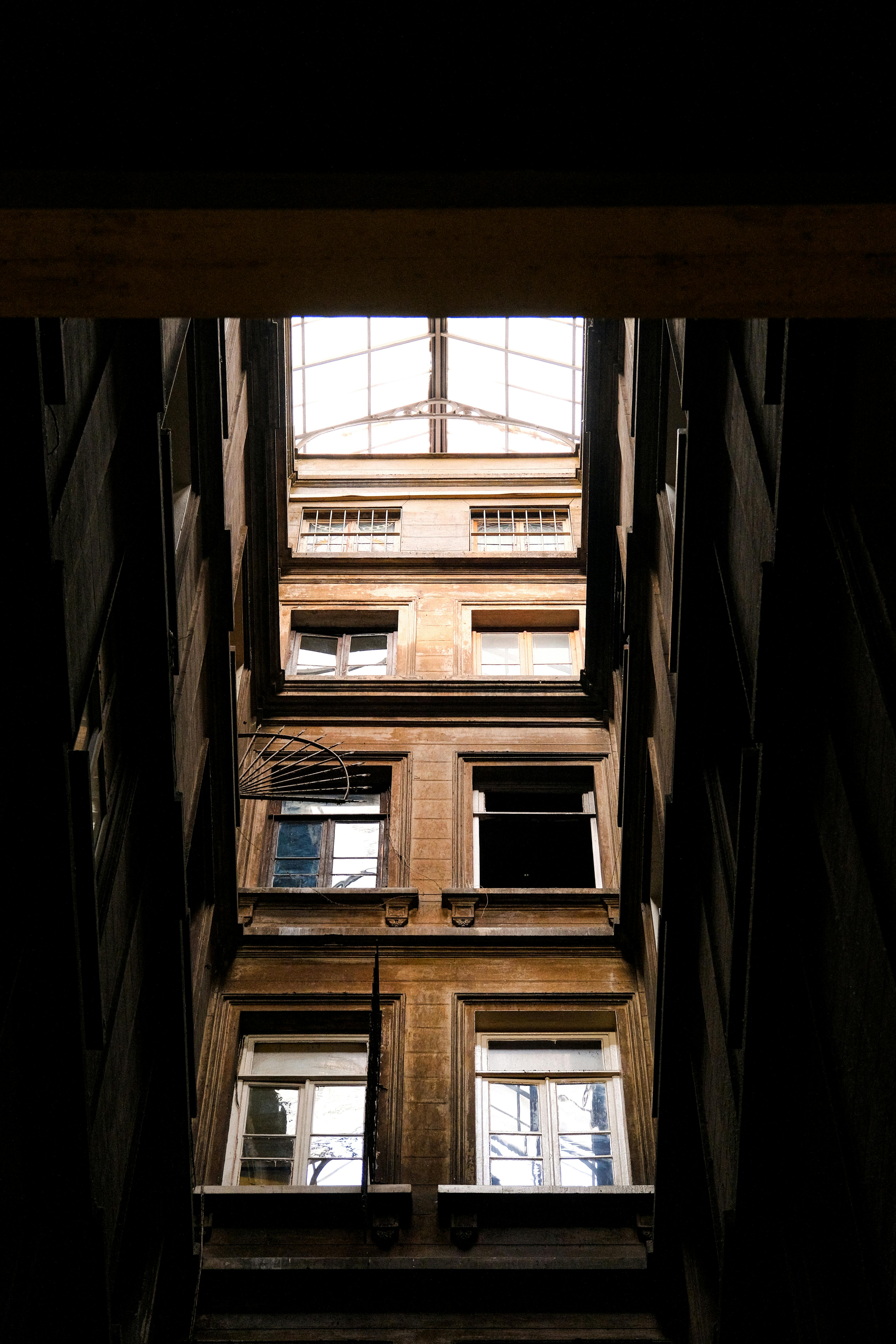 Gratis Mirando hacia arriba en un estrecho patio urbano con ventanas antiguas y un techo de cristal. Foto de stock