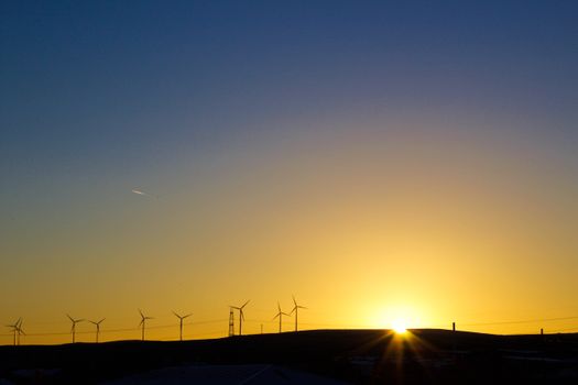 Silhouette of wind turbines against a vibrant sunset sky, capturing renewable energy theme.