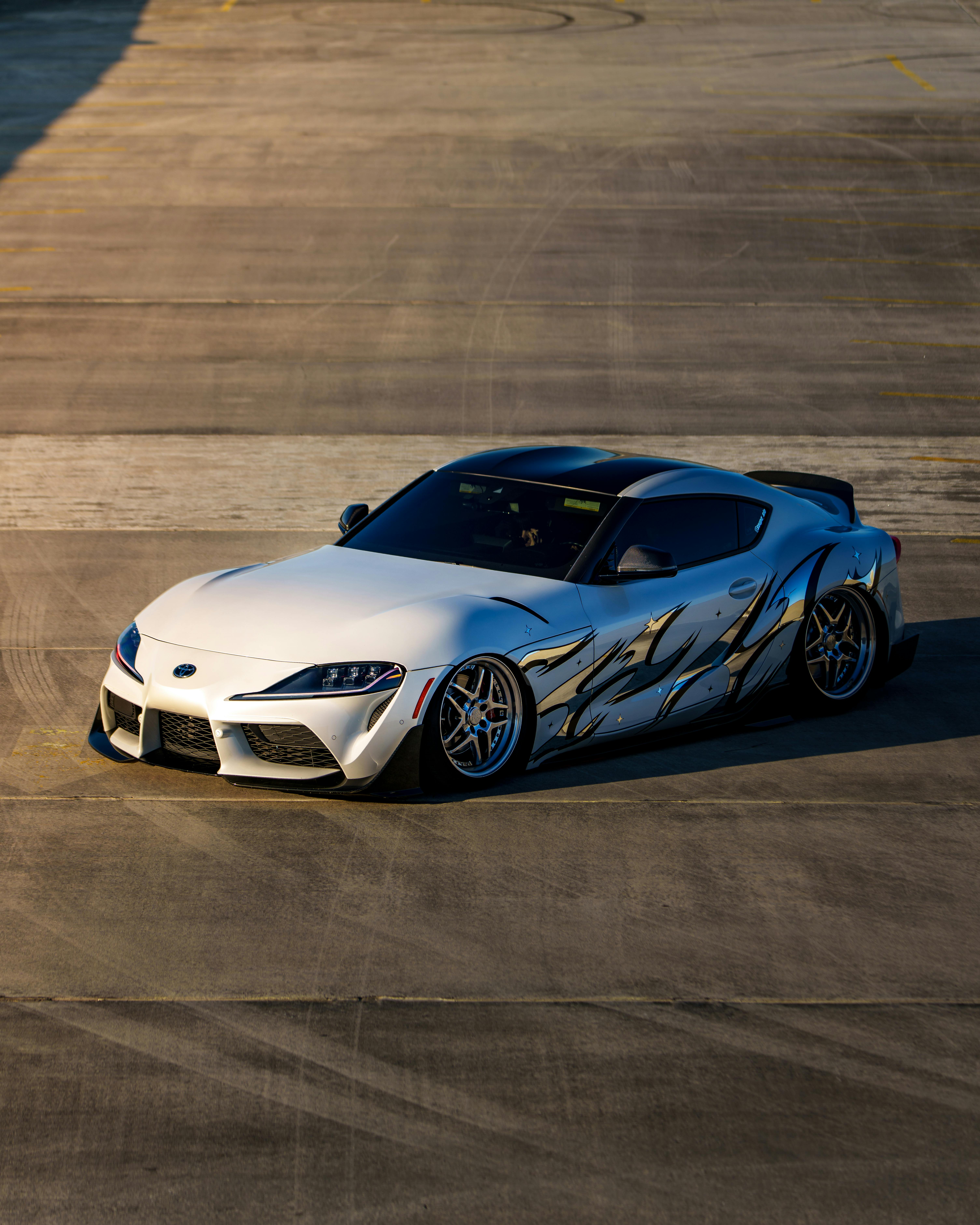 Gratis Auto sportiva bianca con decalcomanie argentate personalizzate su un marciapiede illuminato dal sole. Foto a disposizione