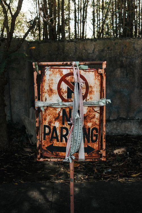 Free Rusty and weathered 'No Parking' sign tied with fabric in an outdoor setting. Stock Photo