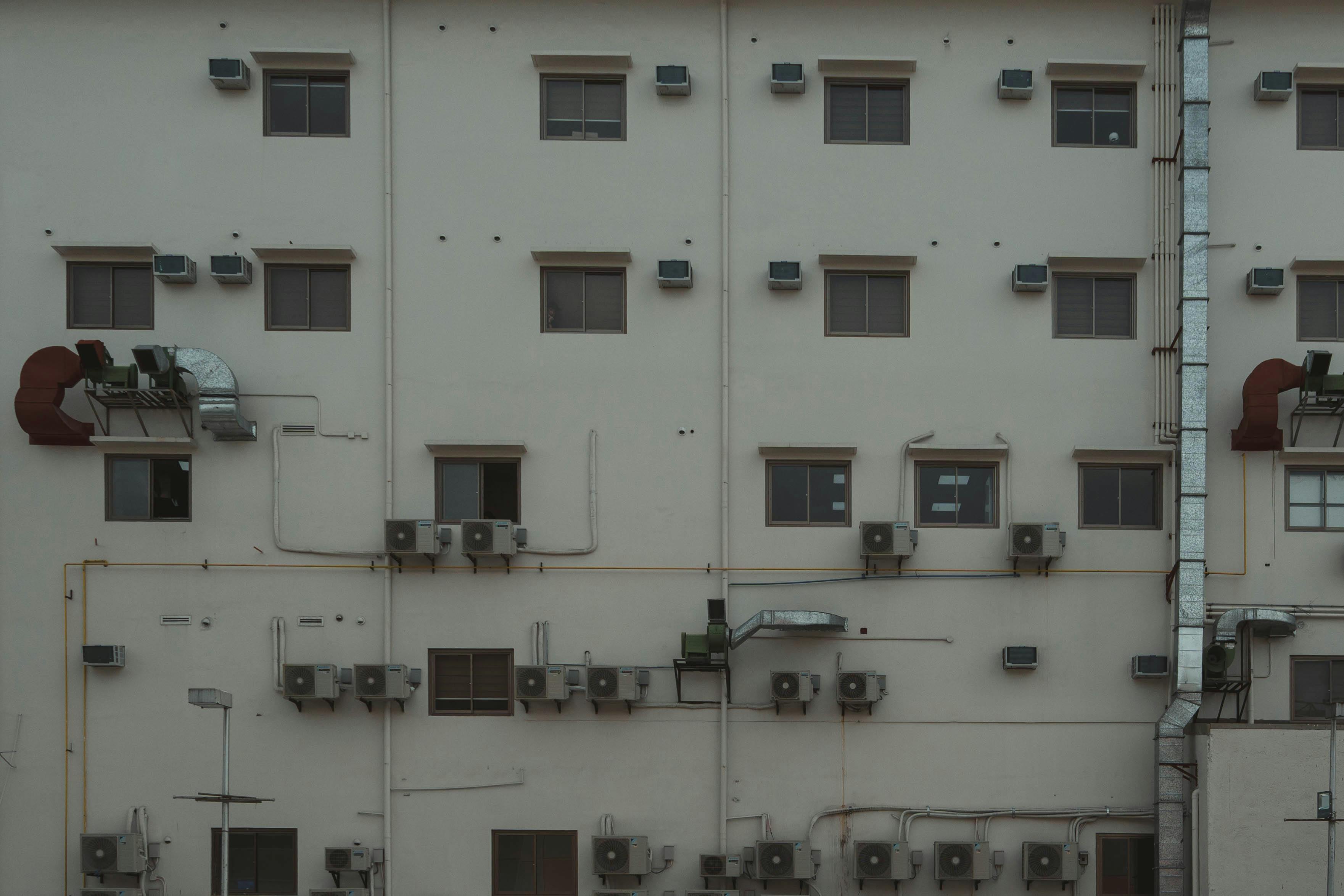 Gratis La facciata di un edificio è ricoperta di unità di aria condizionata e condotti che illustrano l'architettura urbana. Foto a disposizione