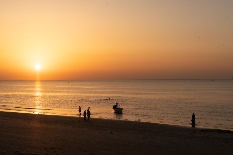 Captivating sunset over Muscat beach with silhouettes and calm waters.