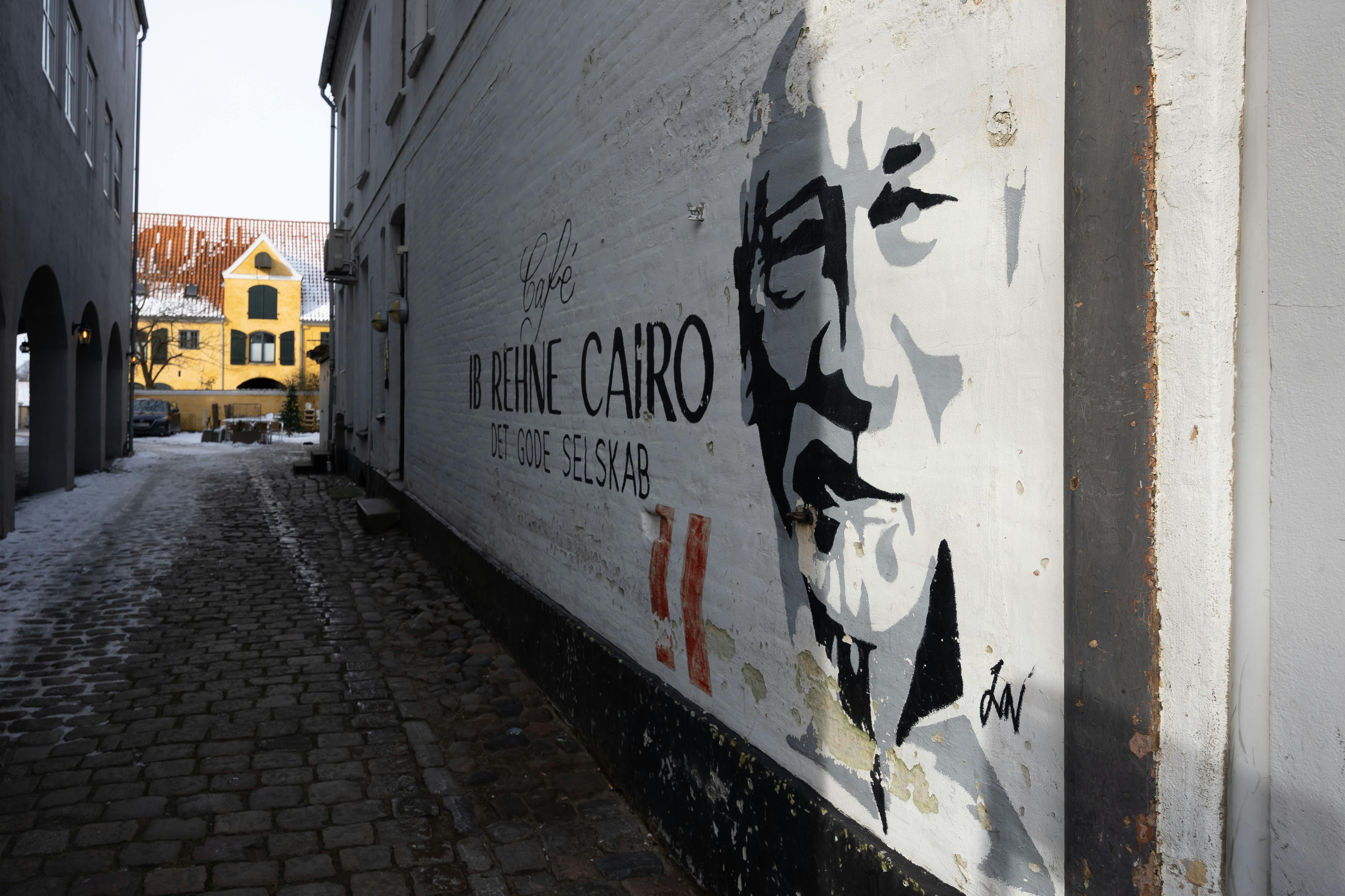 Street art mural in an alleyway of Sønderborg, Denmark, featuring urban graffiti and cobblestone path.