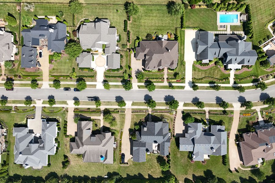 Aerial view of a suburban neighborhood's rooftops, driveways, and tree-lined lawns